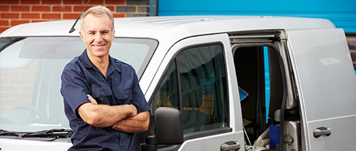 Man with crossed arms next to van with open side door.